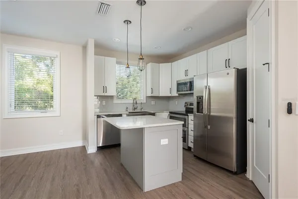 a kitchen with stainless steel appliances granite countertop a refrigerator a sink dishwasher a stove and white countertops with wooden floor