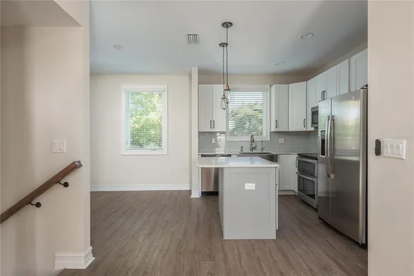 a kitchen with stainless steel appliances a refrigerator a sink dishwasher a stove and white cabinets with wooden floor