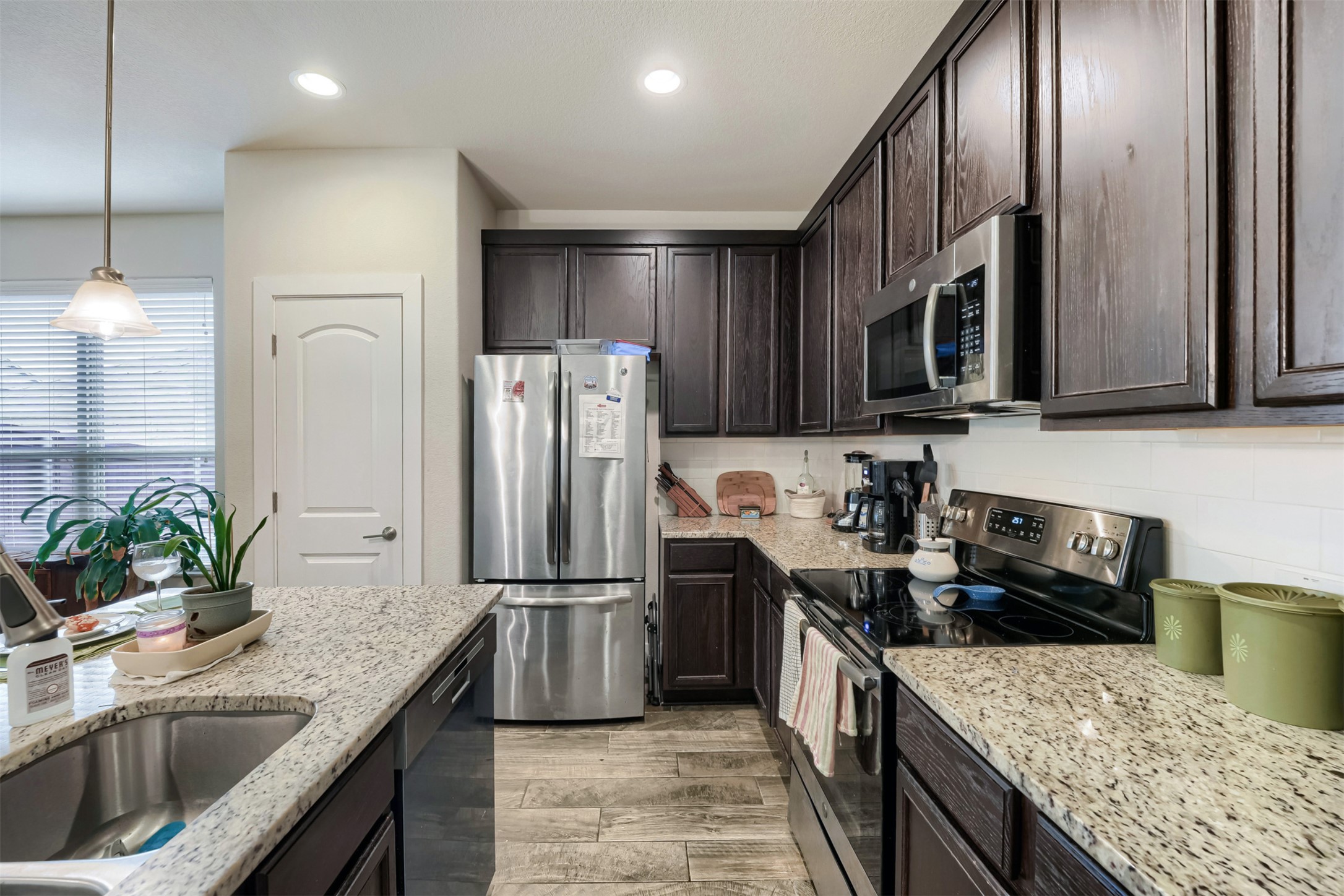 418 High Tech Drive Georgetown, TX 78626 - Photo 11 of 34 Kitchen featuring dark wood cabinetry, light speckled countertops, stainless steel appliances, a tile backsplash, and wood-finish flooring