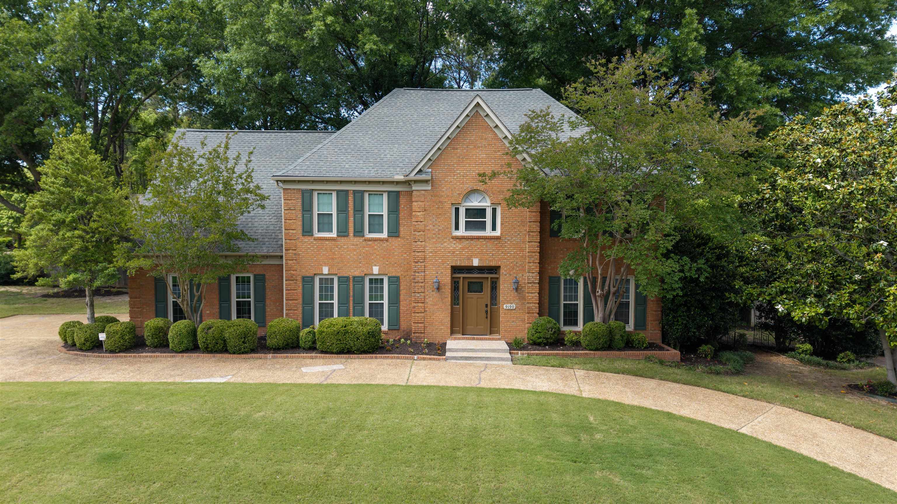 9190 East Bridge Drive Germantown, TN 38139 - Photo 1 of 37 Brick exterior residence featuring a gabled roof, multiple windows with dark shutters, an arched entryway, and a paved circular driveway