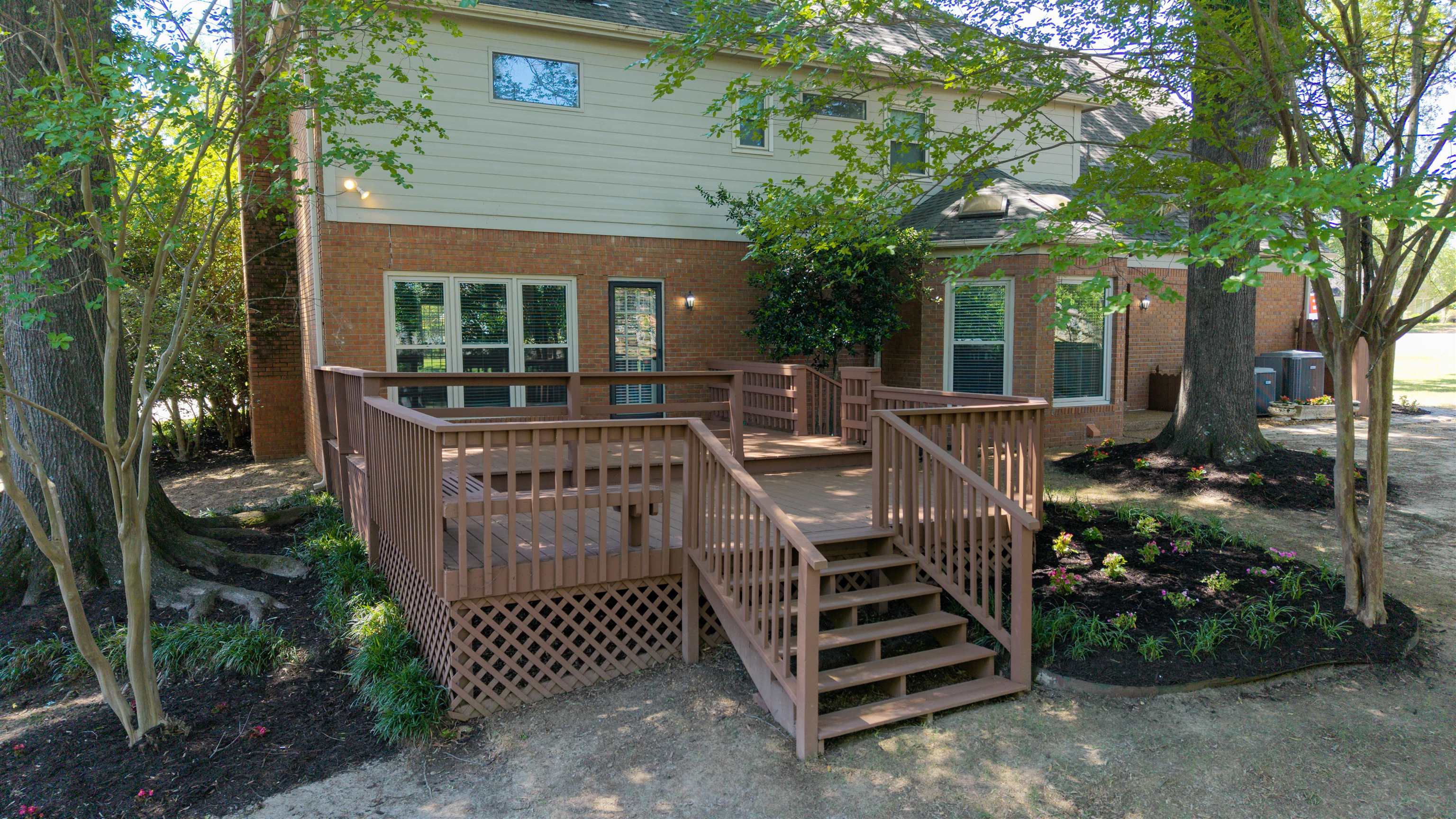 9190 East Bridge Drive Germantown, TN 38139 - Photo 33 of 37 Multi-level wood deck with lattice skirting, brick exterior, and landscaped beds