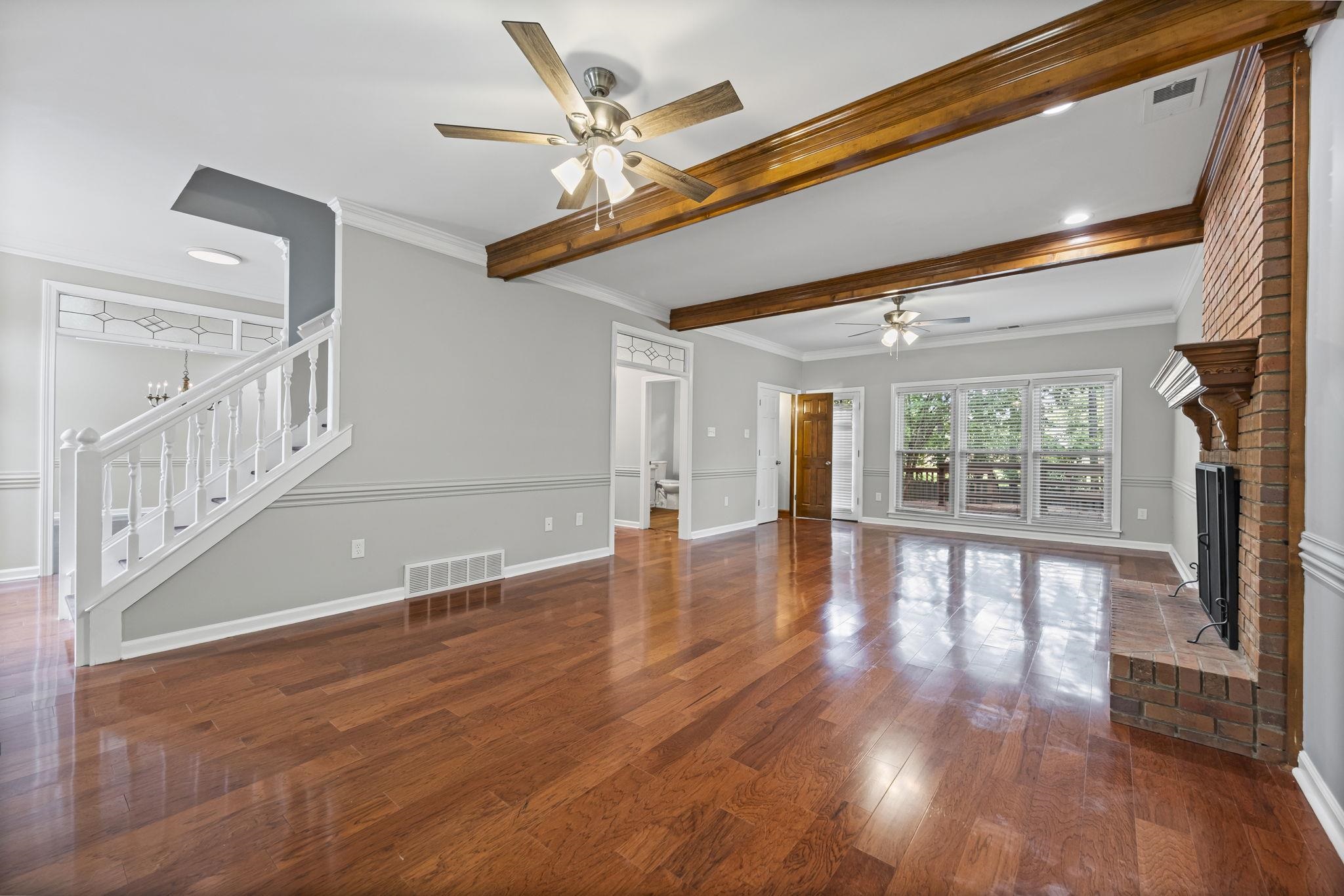 9190 East Bridge Drive Germantown, TN 38139 - Photo 5 of 37 Unfurnished living room featuring crown molding, beamed ceiling, dark wood-type flooring, ceiling fan, and a brick fireplace