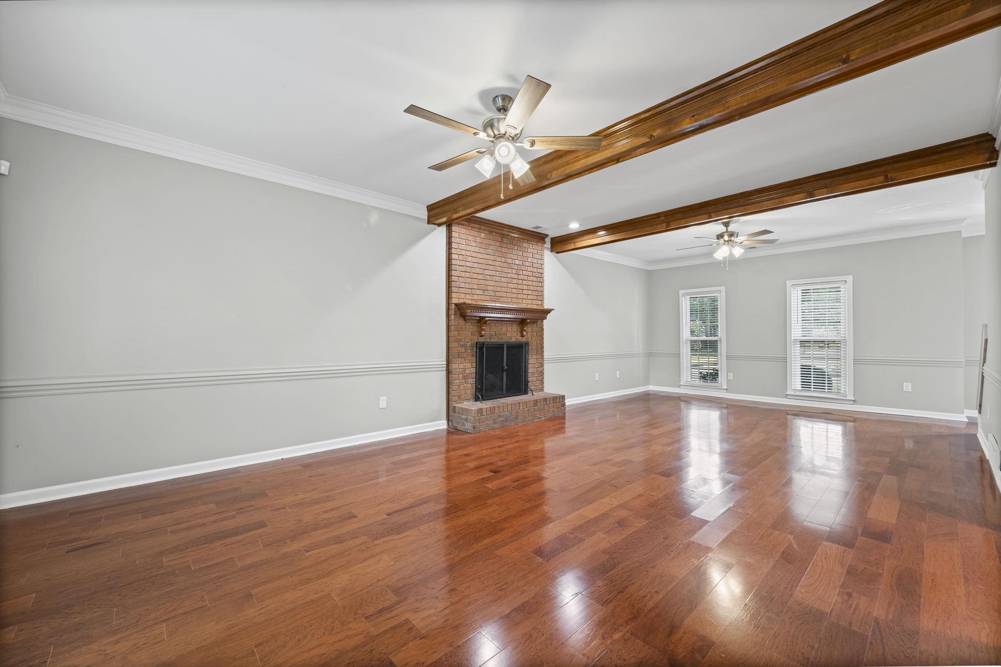 9190 East Bridge Drive Germantown, TN 38139 - Photo 6 of 37 Unfurnished living room with beam ceiling, dark wood-style floors, crown molding, a fireplace, and ceiling fan