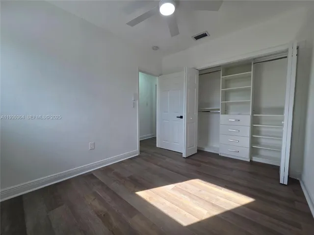 an empty room with wooden floor closet and windows