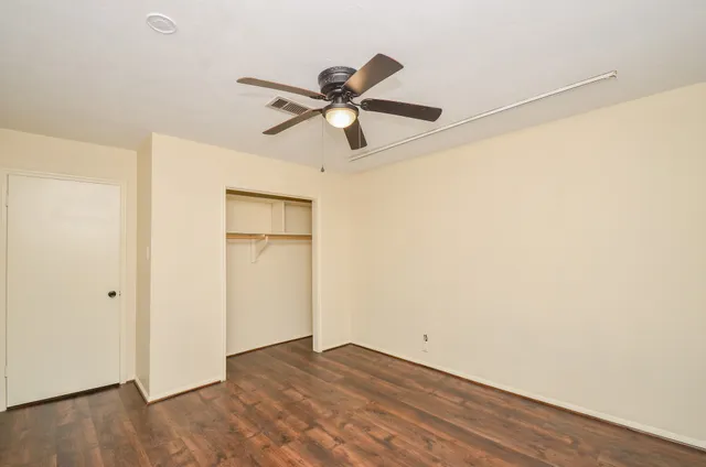 an empty room with wooden floor fan and windows