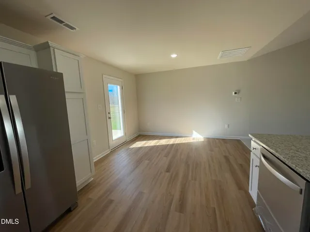 a view of an empty room with wooden floor and a kitchen