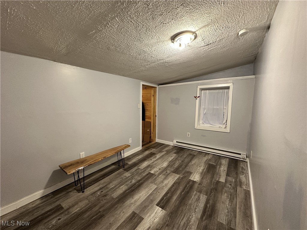 7700 Center Road Ashtabula, OH 44004 - Photo 21 of 31 Empty room with a baseboard heating unit, lofted ceiling, wood finished floors, and a textured ceiling