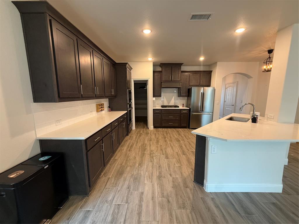 5212 Troupe Road McKinney, TX 75071 - Photo 9 of 38 Spacious kitchen featuring dark wood cabinetry, light-toned countertops, a full stainless steel appliance package, a center island with sink, and wood-finish flooring