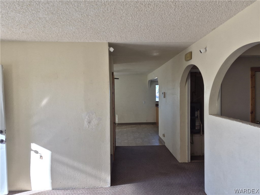 26432 Tamarisk Street, Unit STREET Meadview, AZ 86444 - Photo 8 of 60 Hallway featuring arched walkways, a textured ceiling, and dark colored carpet