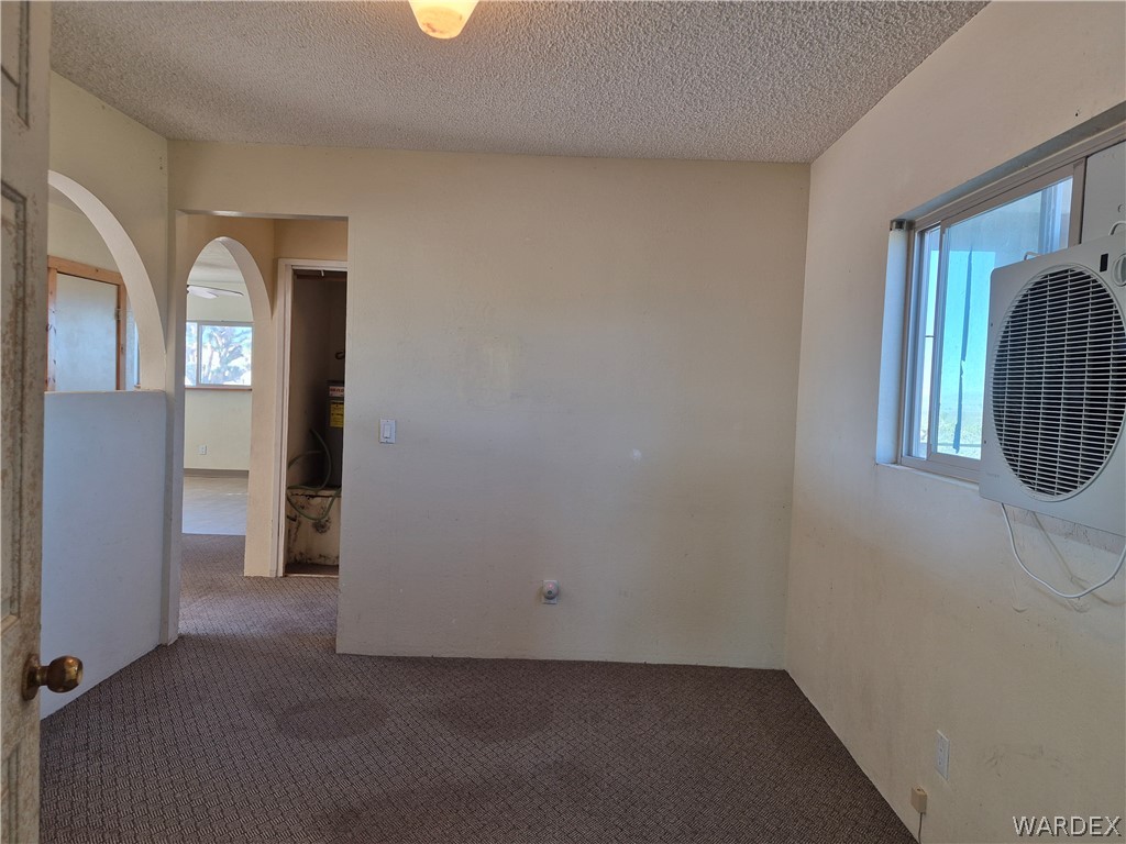 26432 Tamarisk Street, Unit STREET Meadview, AZ 86444 - Photo 9 of 60 Empty room with dark colored carpet, a textured ceiling, and arched walkways