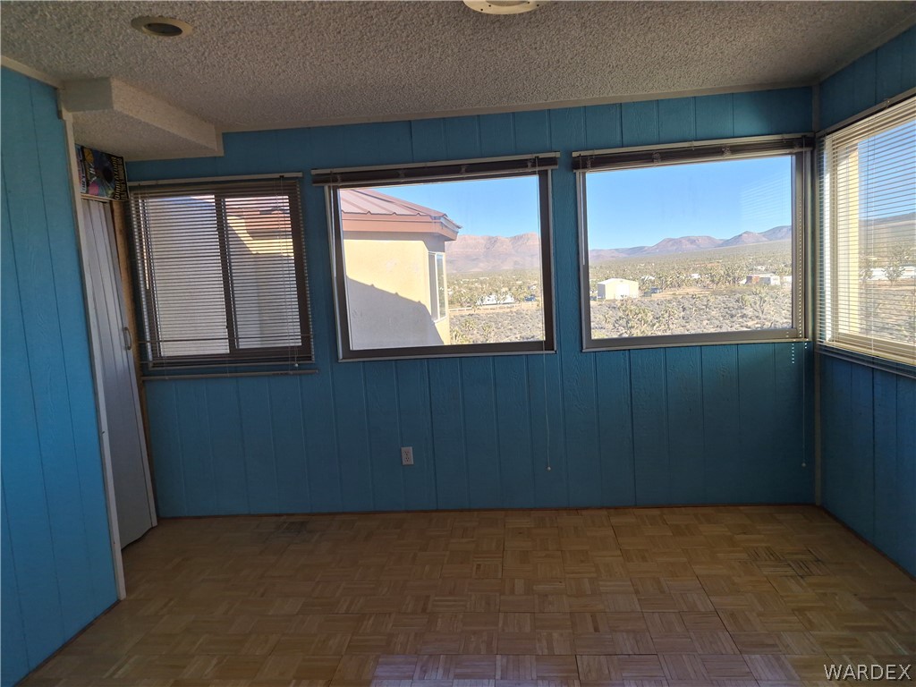 26432 Tamarisk Street, Unit STREET Meadview, AZ 86444 - Photo 31 of 60 Empty room featuring a mountain view, wooden walls, parquet floors, and a textured ceiling