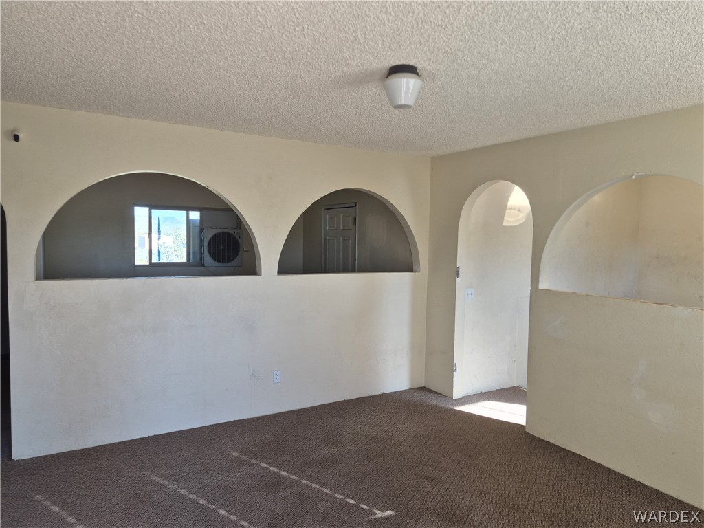 26432 Tamarisk Street, Unit STREET Meadview, AZ 86444 - Photo 4 of 60 Empty room with a textured ceiling, arched walkways, and carpet flooring