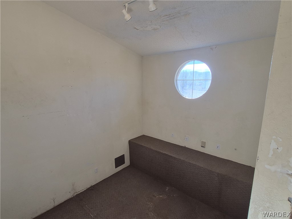 26432 Tamarisk Street, Unit STREET Meadview, AZ 86444 - Photo 6 of 60 Spare room featuring dark colored carpet, a textured ceiling, and rail lighting
