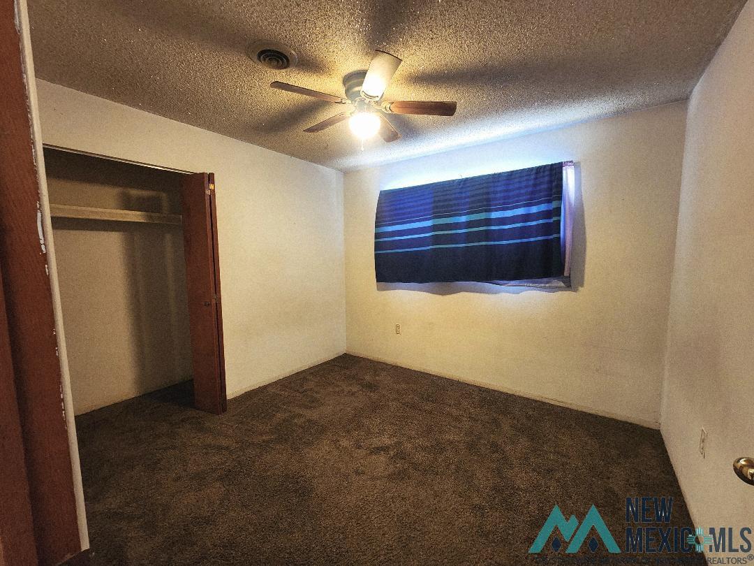 1890 El Portal Road Southeast Deming, NM 88030 - Photo 8 of 21 Unfurnished bedroom with dark colored carpet, a textured ceiling, a ceiling fan, and a closet