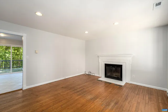an empty room with wooden floor fireplace and windows