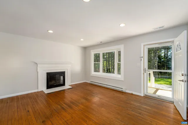 an empty room with wooden floor fireplace and windows