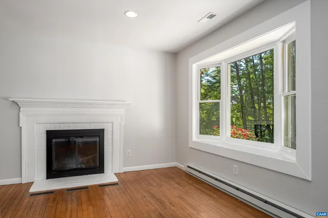 a view of an empty room with wooden floor fireplace and a window