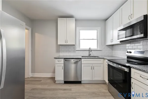 a kitchen with stainless steel appliances granite countertop white cabinets sink and a microwave