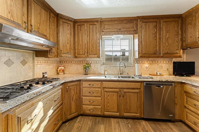 a kitchen with stainless steel appliances granite countertop a refrigerator a sink dishwasher a stove and white countertops with wooden floor