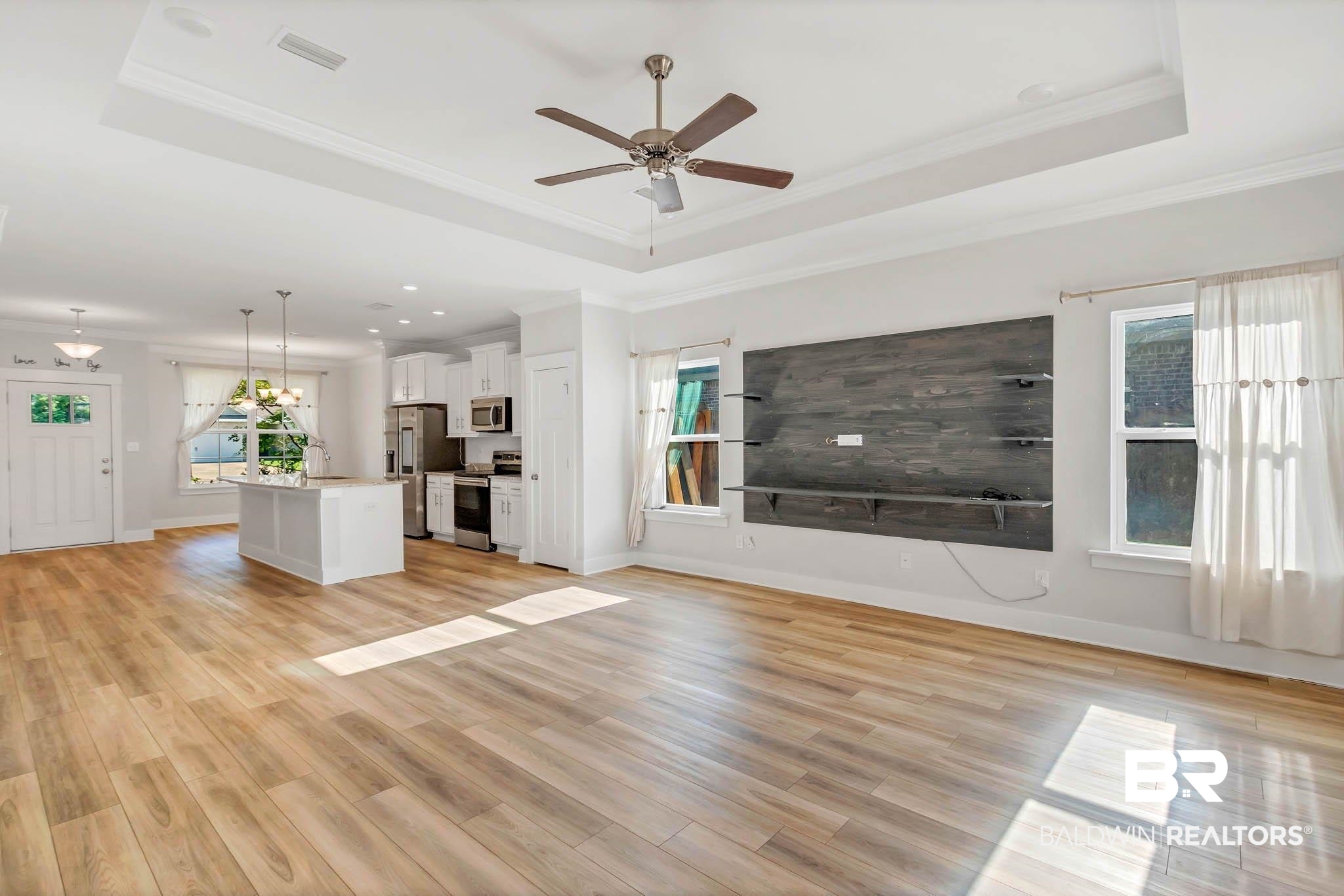 16461 Prado Loop Loxley, AL 36551 - Photo 19 of 78 Unfurnished living room featuring a raised ceiling, ornamental molding, plenty of natural light, a ceiling fan, and light wood-style floors