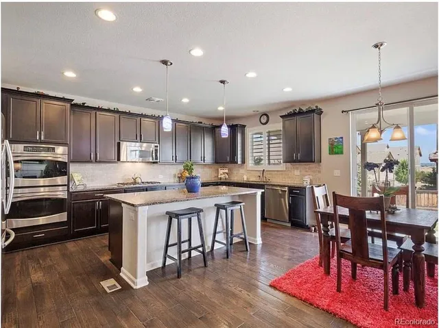 a kitchen with stainless steel appliances granite countertop a stove top oven a sink a dining table and chairs with wooden floor