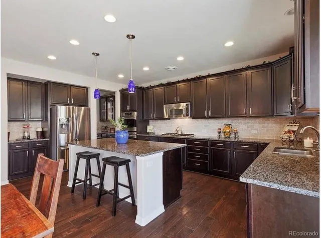 a kitchen with granite countertop stainless steel appliances a sink a stove a refrigerator cabinets and a center island