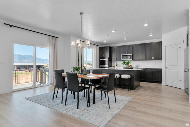 1418 West 2350th South, Unit 15 Perry, UT 84302 - Photo 7 of 22 Open-concept living area featuring light wood-finish flooring, a modern dining light fixture, a spacious kitchen island with seating, dark cabinetry, and integrated stainless steel appliances