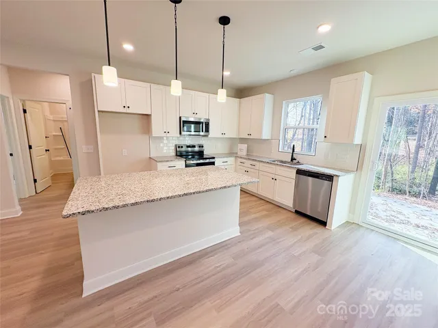 a large kitchen with stainless steel appliances kitchen island granite countertop a stove a sink a refrigerator a center island and wooden floor