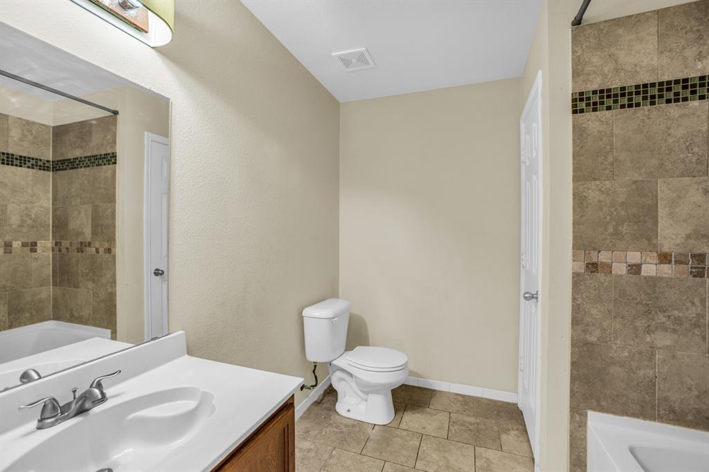 5718 Green Ivy Road Denton, TX 76210 - Photo 26 of 37 Bathroom featuring a vanity with a white countertop and wood-finish cabinetry, a toilet, a shower-tub combination with tiled walls, and tiled flooring
