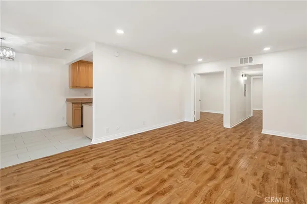 a view of empty room with wooden floor and kitchen