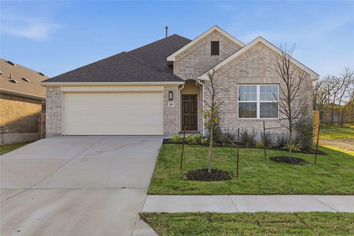 Ranch-style house with concrete driveway, brick siding, a front yard, a garage, and roof with shingles