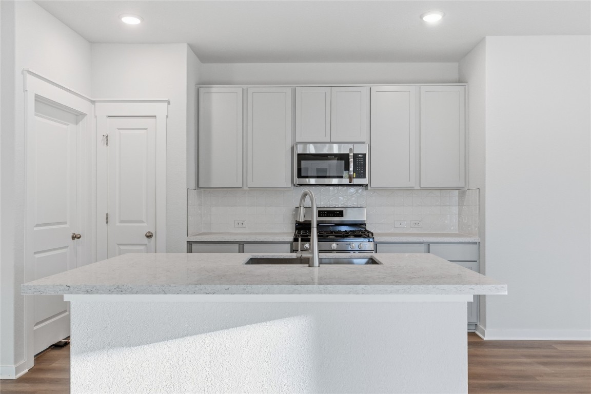 350 Mustang Bend Kyle, TX 78640 - Photo 5 of 18 Kitchen with stainless steel appliances, a kitchen island with sink, light stone counters, decorative backsplash, and light wood-type flooring