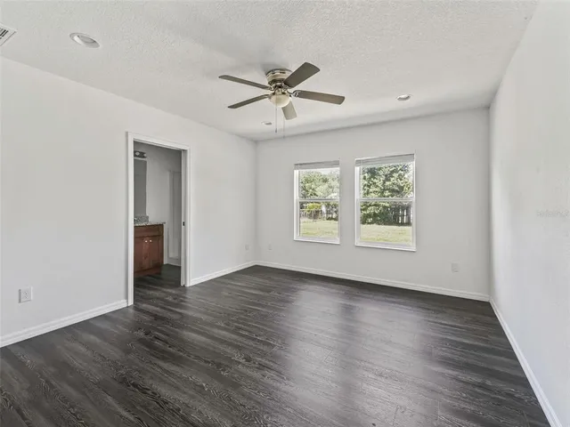 an empty room with wooden floor a ceiling fan and windows