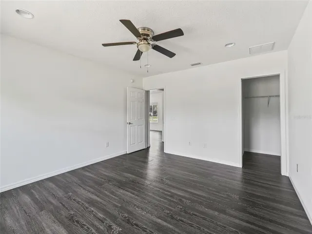 a view of an empty room with wooden floor and a ceiling fan
