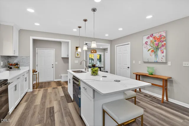 a large white kitchen with a stove a sink a dining table and chairs with wooden floor