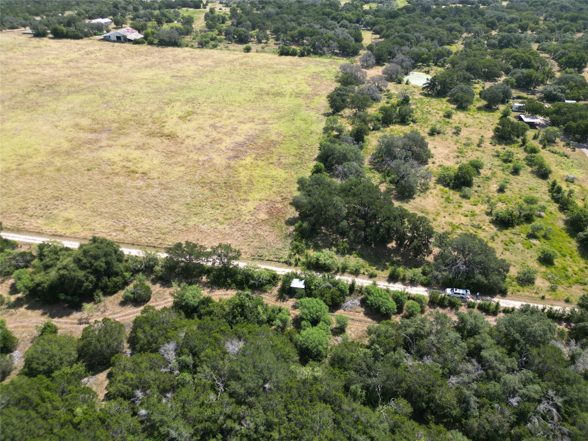 200/ Shady Grove Road Bertram, TX 78605 - Photo 17 of 17 A rural landscape featuring a dirt road, open fields, and abundant natural foliage.