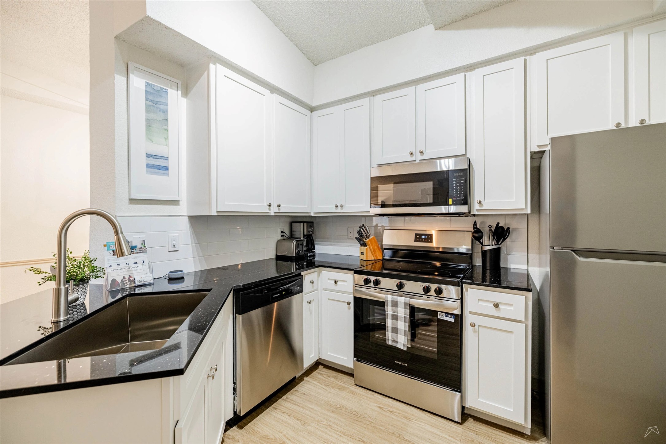 11908 Anderson Mill Road, Unit 822 Austin, TX 78726 - Photo 17 of 23 Kitchen featuring stainless steel appliances, dark stone counters, white cabinets, a textured ceiling, and light wood-type flooring