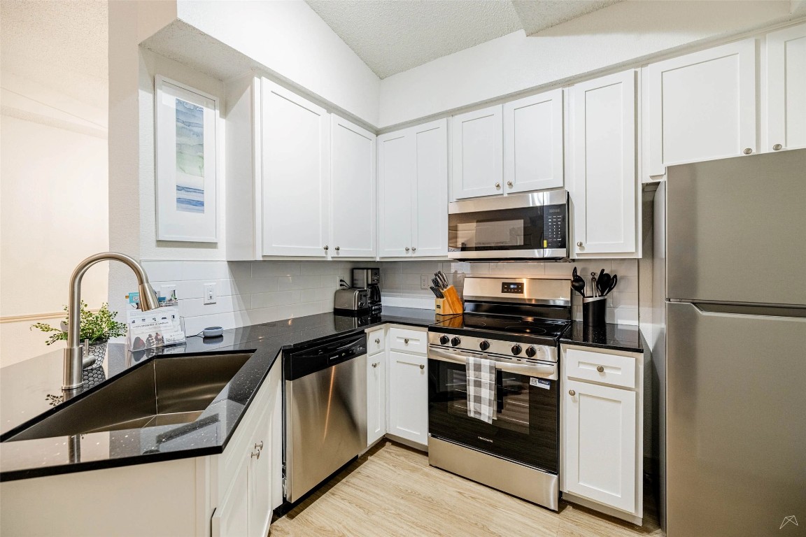 11908 Anderson Mill Road, Unit 822 Austin, TX 78726 - Photo 17 of 23 Kitchen featuring stainless steel appliances, dark stone counters, white cabinets, a textured ceiling, and light wood-type flooring