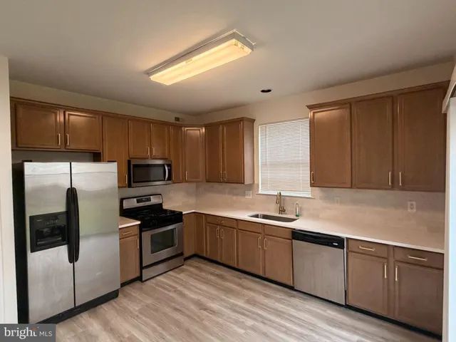 a kitchen with stainless steel appliances granite countertop a sink a stove a refrigerator with grey cabinets and wooden floor