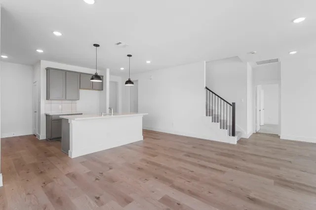 a view of an empty room with wooden floor and a kitchen