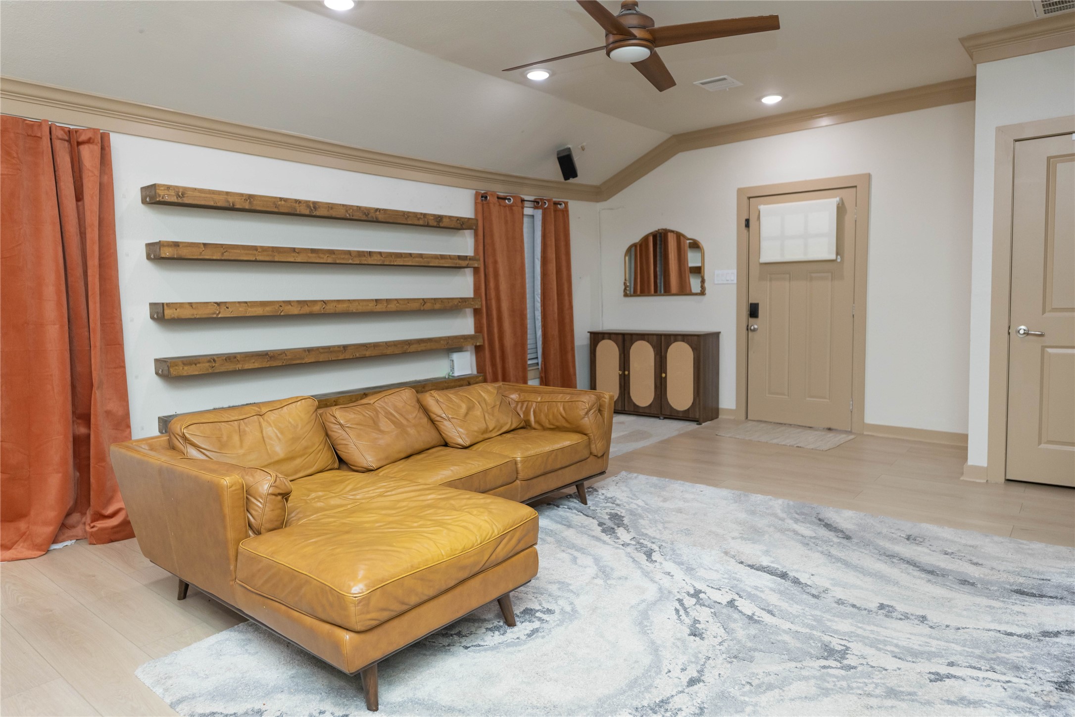 8007 Capitol Street Houston, TX 77012 - Photo 8 of 25 This spacious living room features, rustic floating shelves, and orange curtains. It has a modern ceiling fan, light wood flooring, and a neutral color palette, creating an inviting atmosphere.