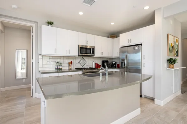 a kitchen with stainless steel appliances granite countertop a refrigerator a stove a sink a microwave and white cabinets with wooden floor