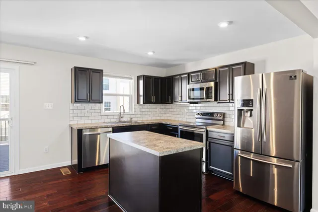 a kitchen with stainless steel appliances granite countertop a refrigerator a sink dishwasher a stove top oven a oven with wooden floor