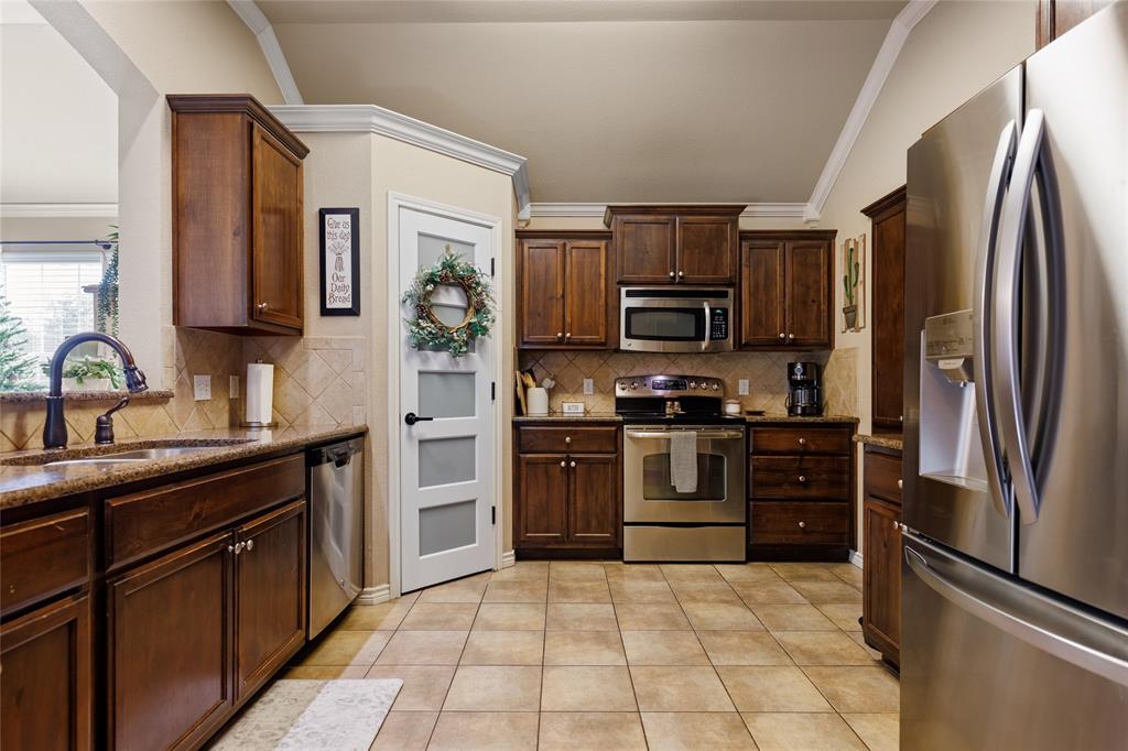 2565 Paddock Lane Robinson, TX 76706 - Photo 10 of 32 Kitchen with appliances with stainless steel finishes, dark stone countertops, crown molding, light tile patterned floors, and dark brown cabinetry
