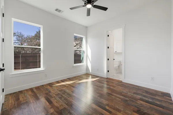 an empty room with wooden floor chandelier fan and windows