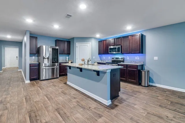 a kitchen with stainless steel appliances granite countertop a stove a sink dishwasher a refrigerator and a microwave oven with wooden floor