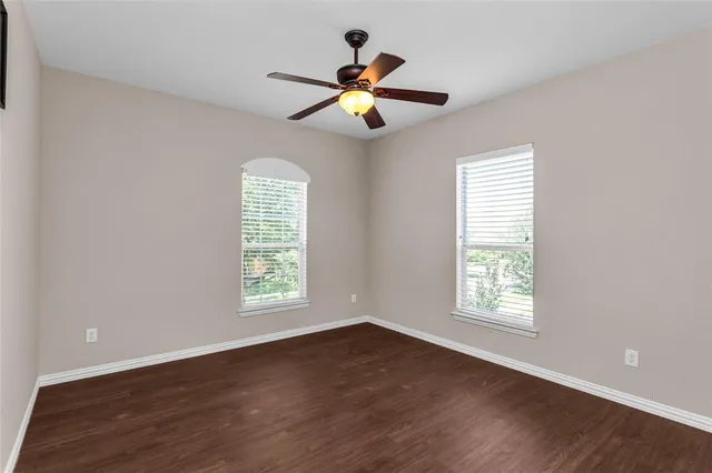 an empty room with wooden floor fan and windows
