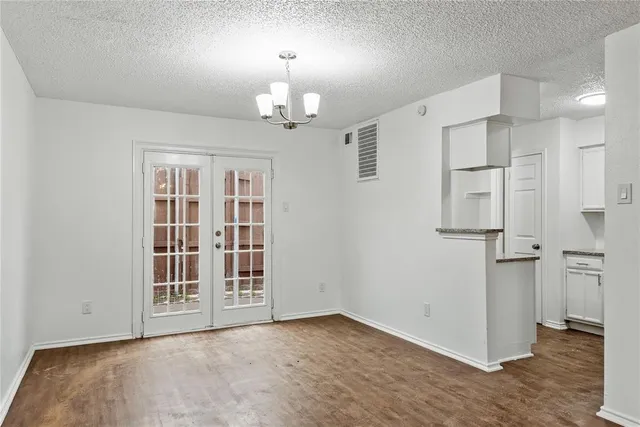 an empty room with wooden floor chandelier and windows