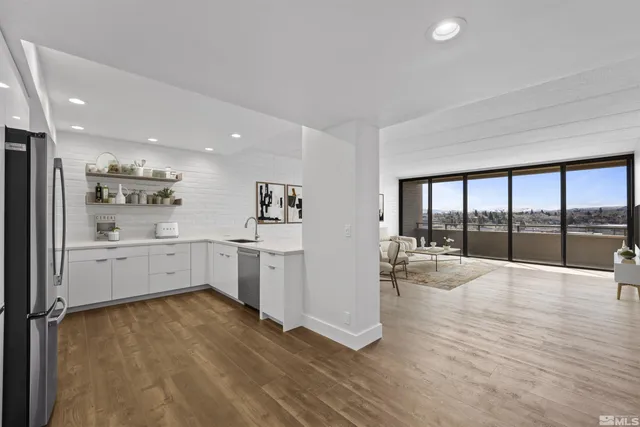 a view of an empty room and kitchen with wooden floor