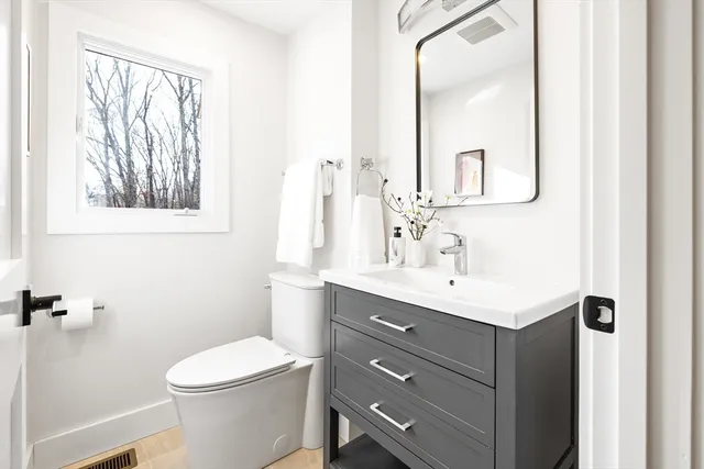 a bathroom with a toilet a sink a mirror a window and vanity